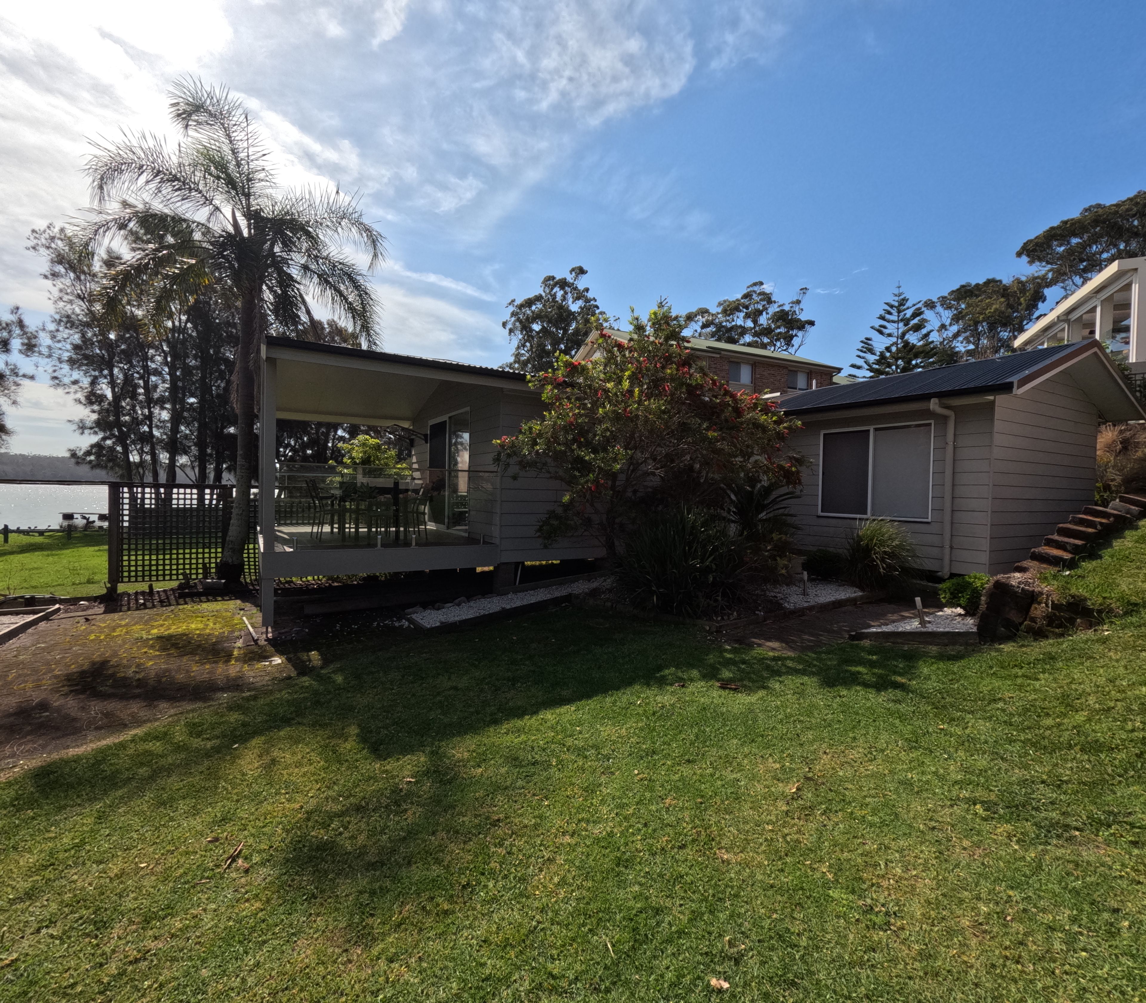 A residential property with a covered outdoor seating area, a well-maintained lawn, and a view of the surrounding landscape.