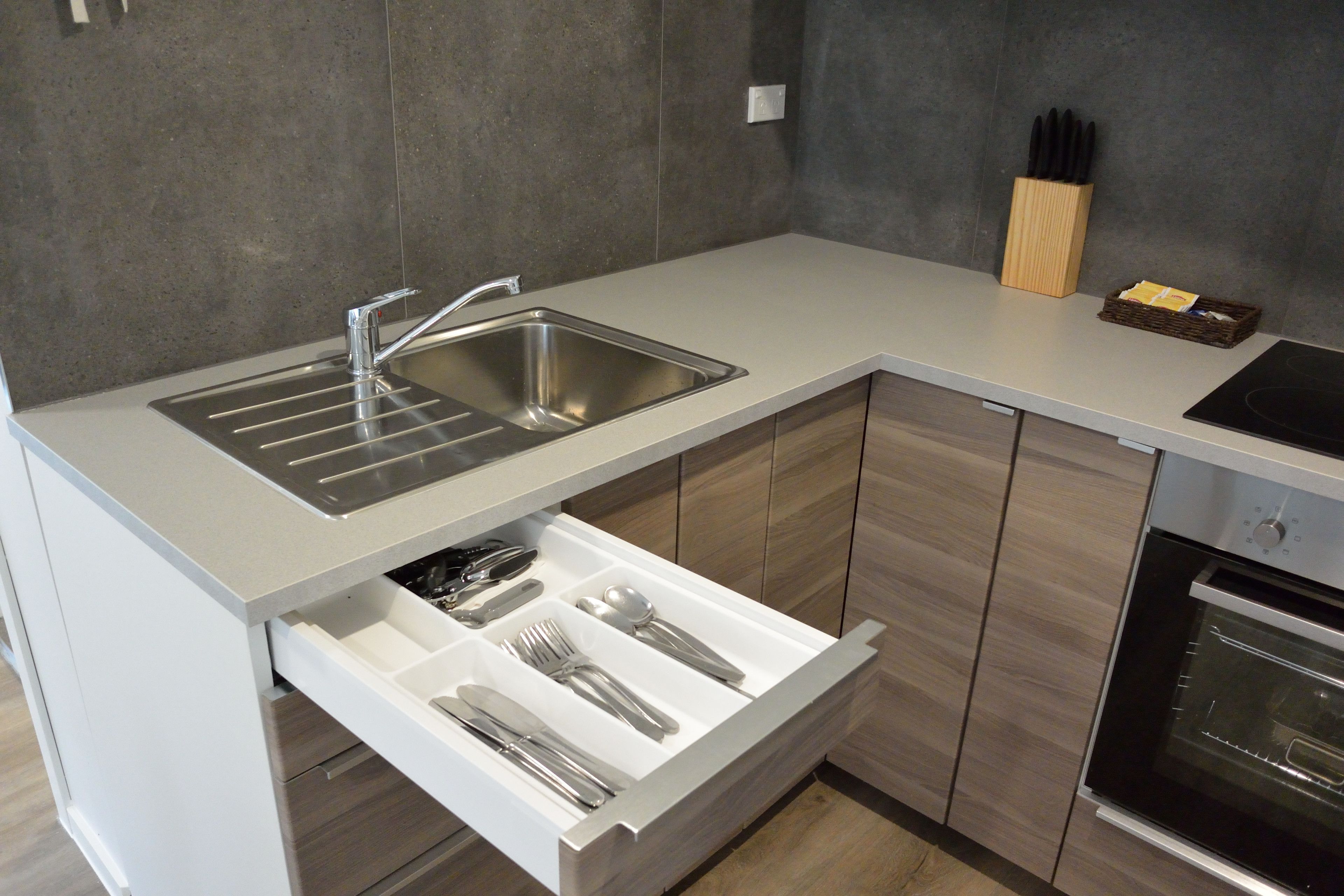 A modern kitchen with a stainless steel sink, a built-in oven, and a drawer organizer for utensils.