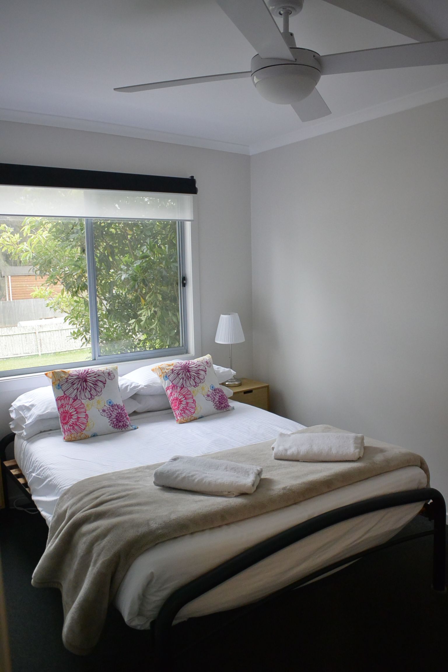 A bedroom with a bed, pillows, a bedside lamp, a window, and a ceiling fan.