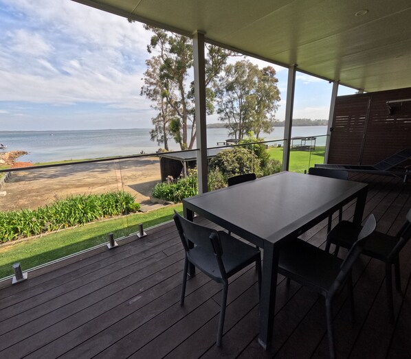 Un espacio al aire libre cubierto con una mesa y sillas, con vistas a una playa y un lago.