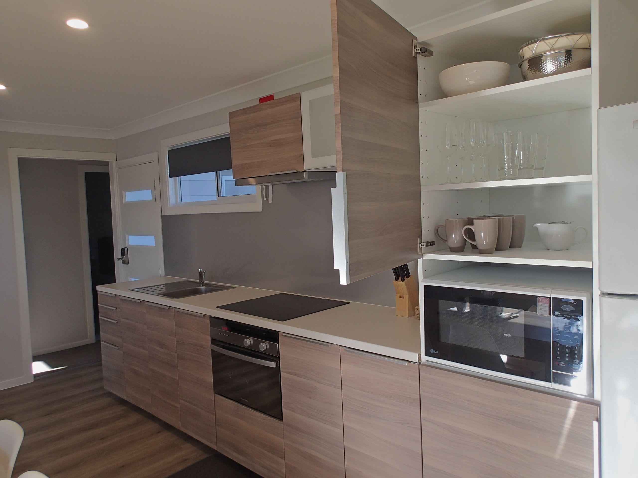 A modern kitchen with wooden cabinets, a built-in oven, a microwave, and a sink.