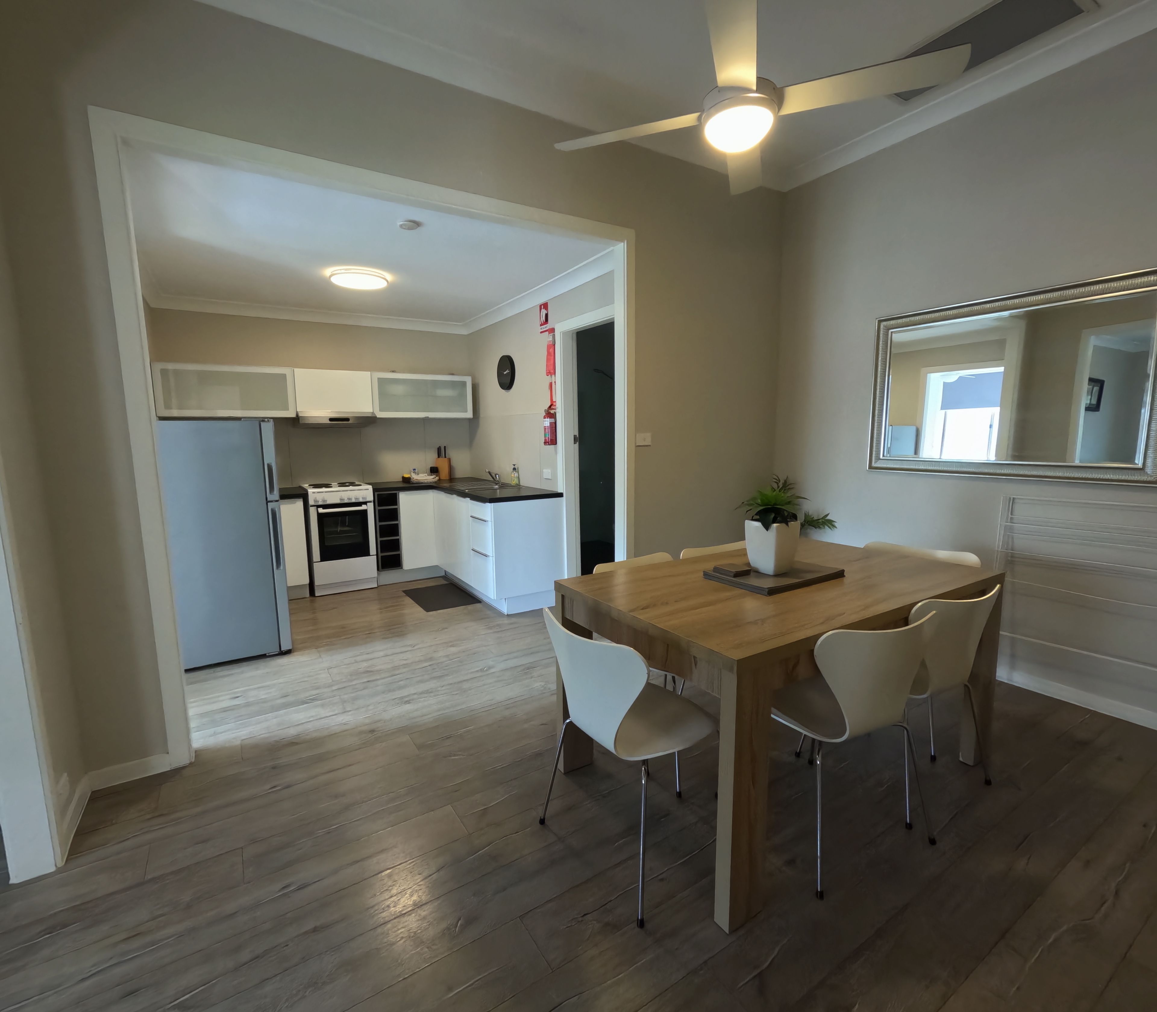 A modern kitchen with white cabinets, a stove, and a refrigerator. There is a dining area with a wooden table and chairs.