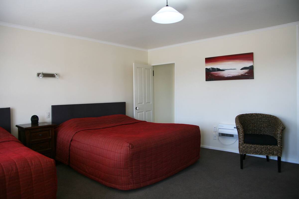 Habitación de hotel con dos camas, una silla, un escritorio, una lámpara y un cuadro en la pared.
