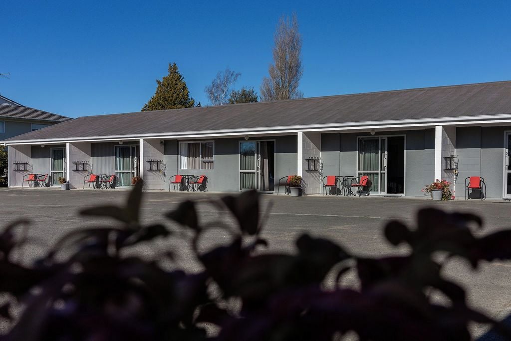 A motel with multiple rooms, each with a door and window, and a parking lot in front.