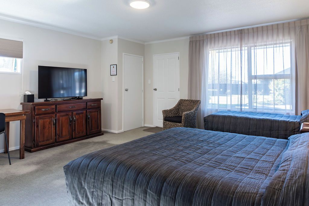 A bedroom with a large bed, a television on a wooden cabinet, a chair, and a window with curtains.