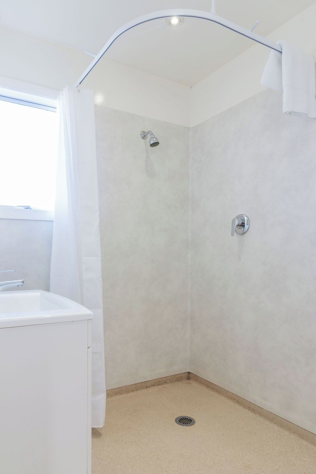 A bathroom with a shower, a sink, and a window.