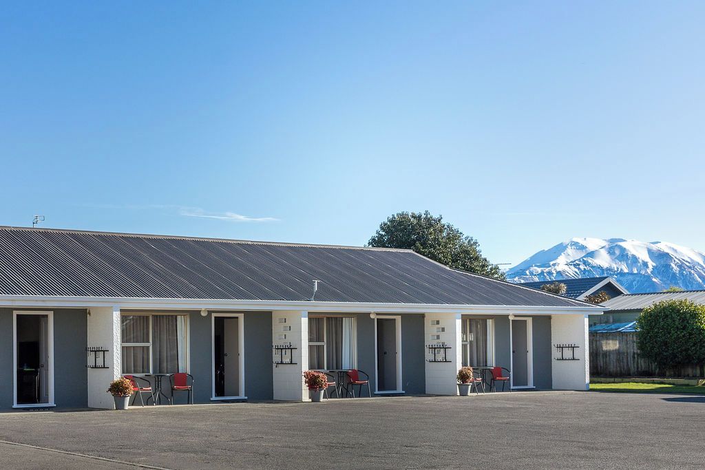 A motel with a row of rooms, each with a door and a small window. There is a mountain in the background.