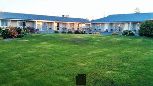 A motel with a large lawn in front, multiple rooms with balconies, and a blue roof. - Mount Hutt Motels (Methven)