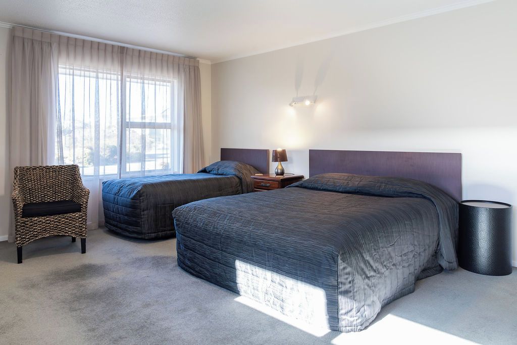 Camera d'albergo con due letti, una sedia, un comodino con una lampada e una finestra con tende.