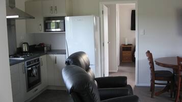 A compact kitchen with a stove, oven, microwave, and refrigerator. There is a dining area with a wooden table and chairs.