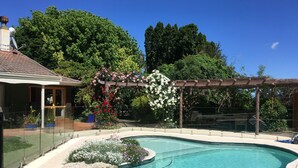 A swimming pool with a pergola and flower arrangements, surrounded by a fence and trees. - Bluebell Lodge And Cottage (Hastings)