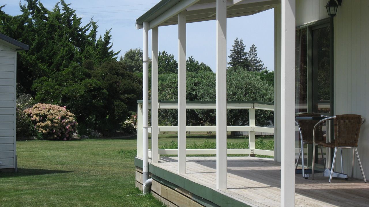 Un porche cubierto con una terraza de madera, una silla y vistas a un jardín y árboles.