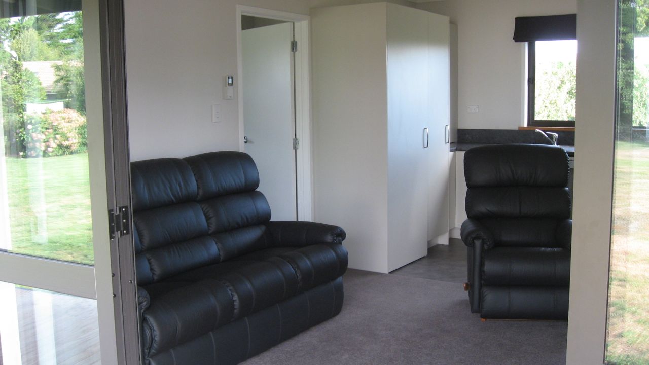A room with a black leather sofa and a recliner, a white door, and a view of a garden through a glass door.