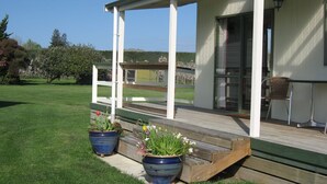 A covered porch with a wooden deck, a chair, and potted plants. - Bluebell Lodge And Cottage (Hastings)