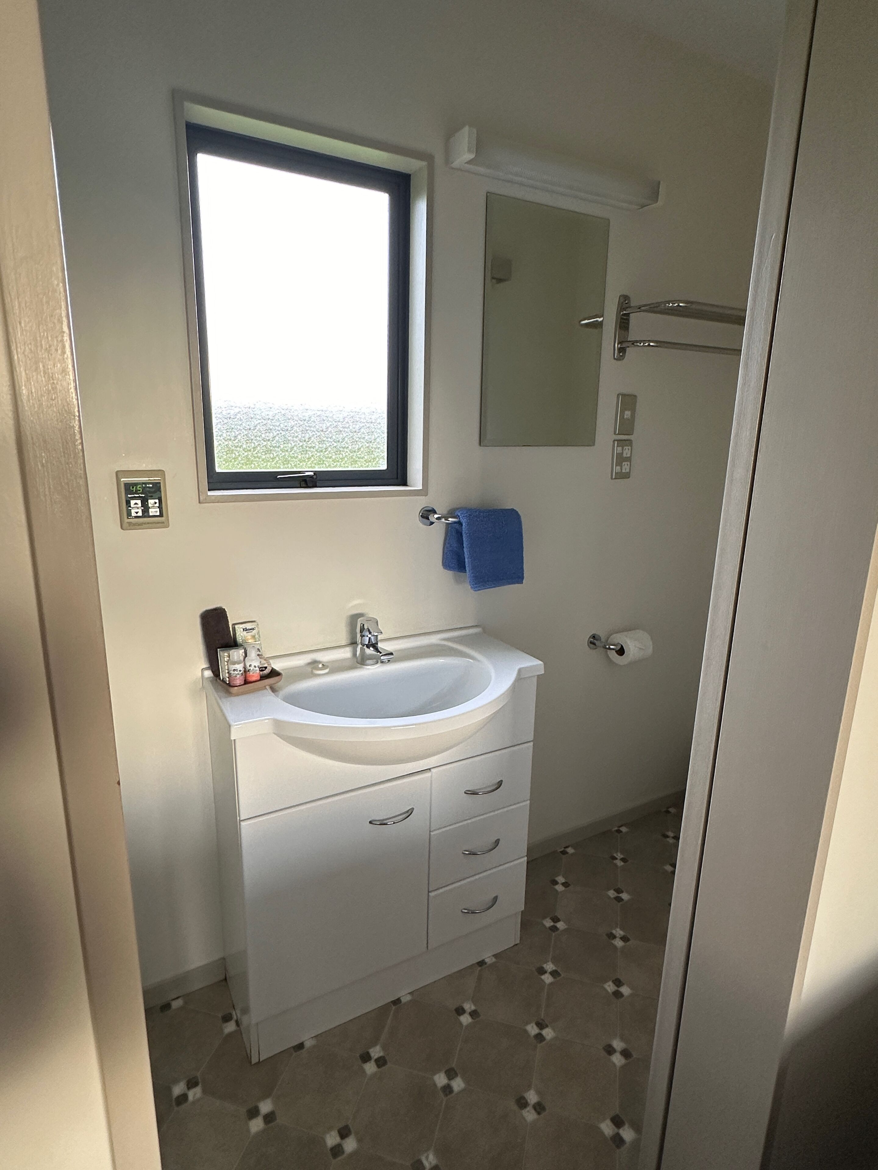 Een badkamer met een wit wastafelmeubel, een raam, een spiegel en een handdoekhouder.