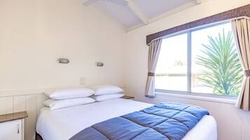 A bedroom with a bed, a window with curtains, a ceiling fan, and a small bedside table.