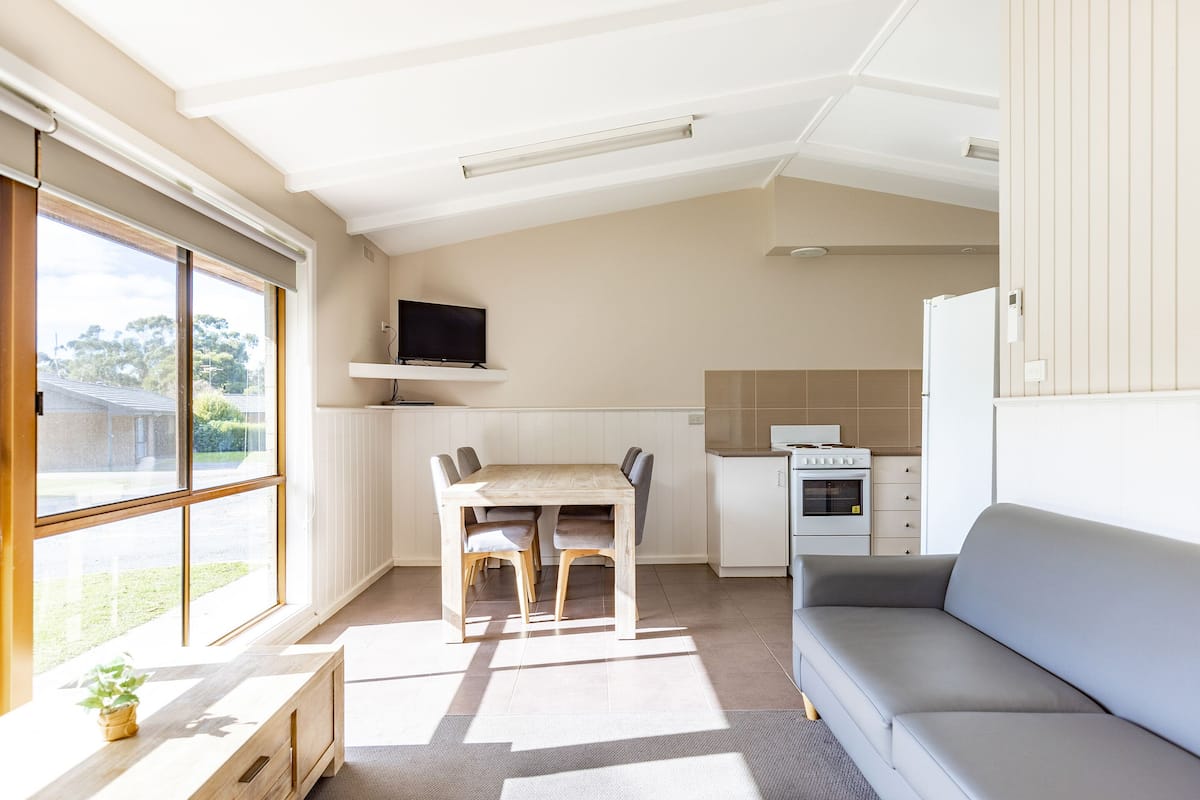 A modern kitchen with a dining table and chairs, a built-in TV, and a grey sofa.