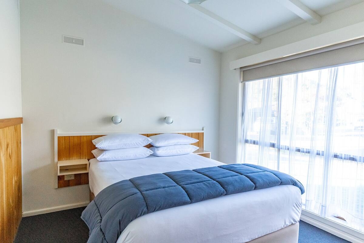 A neatly made bed with a blue blanket, white pillows, and a wooden headboard.