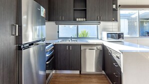 Une cuisine moderne avec des meubles de couleur sombre, des appareils électroménagers en acier inoxydable et une fenêtre qui laisse entrer la lumière naturelle.