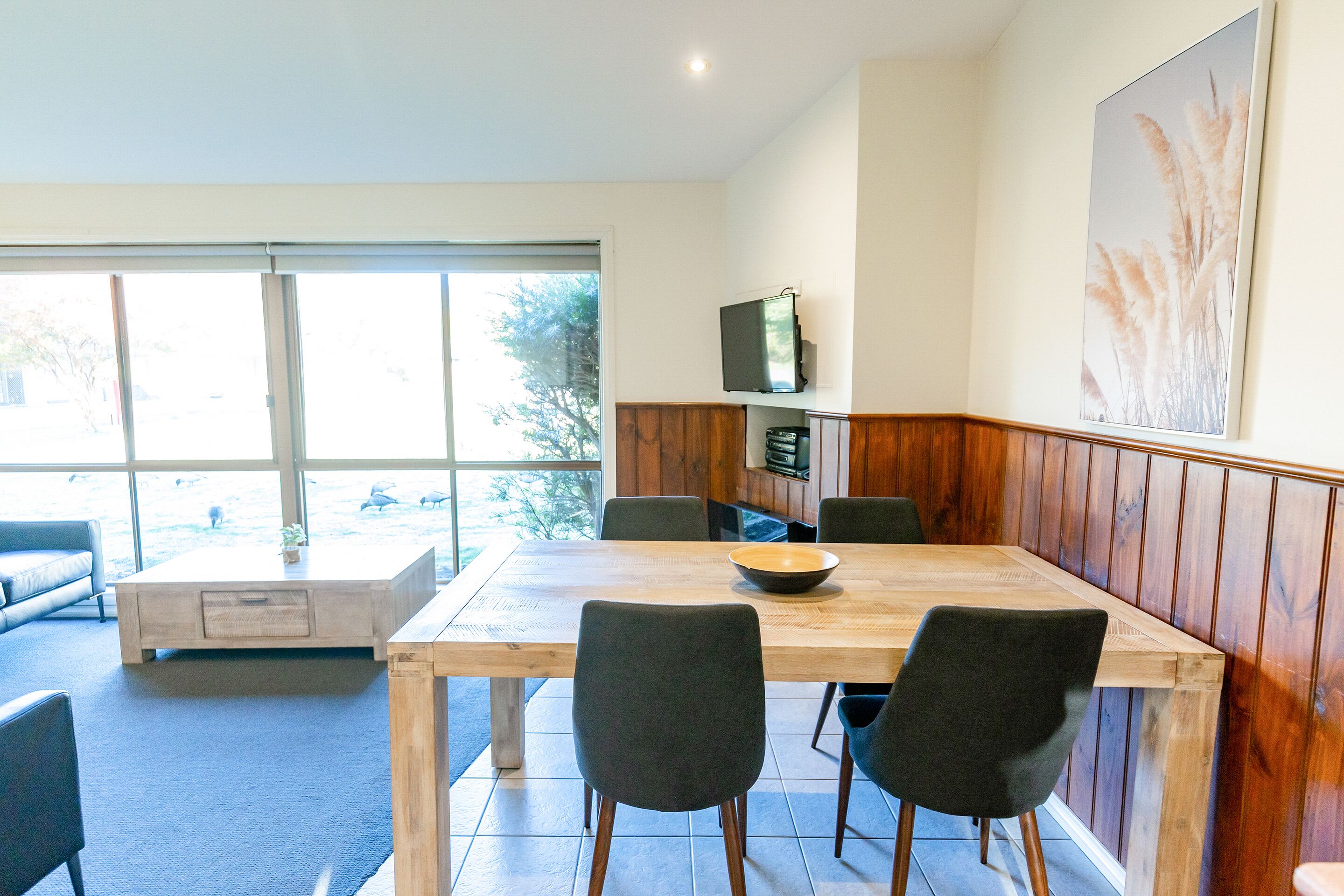 Un comedor con una mesa de madera, seis sillas y un televisor en la pared.