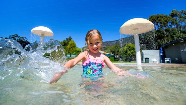 Un enfant joue dans une fontaine ou un bassin avec deux grands parasols.