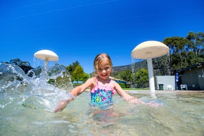 Niño jugando en una fuente de agua con dos sombrillas grandes.