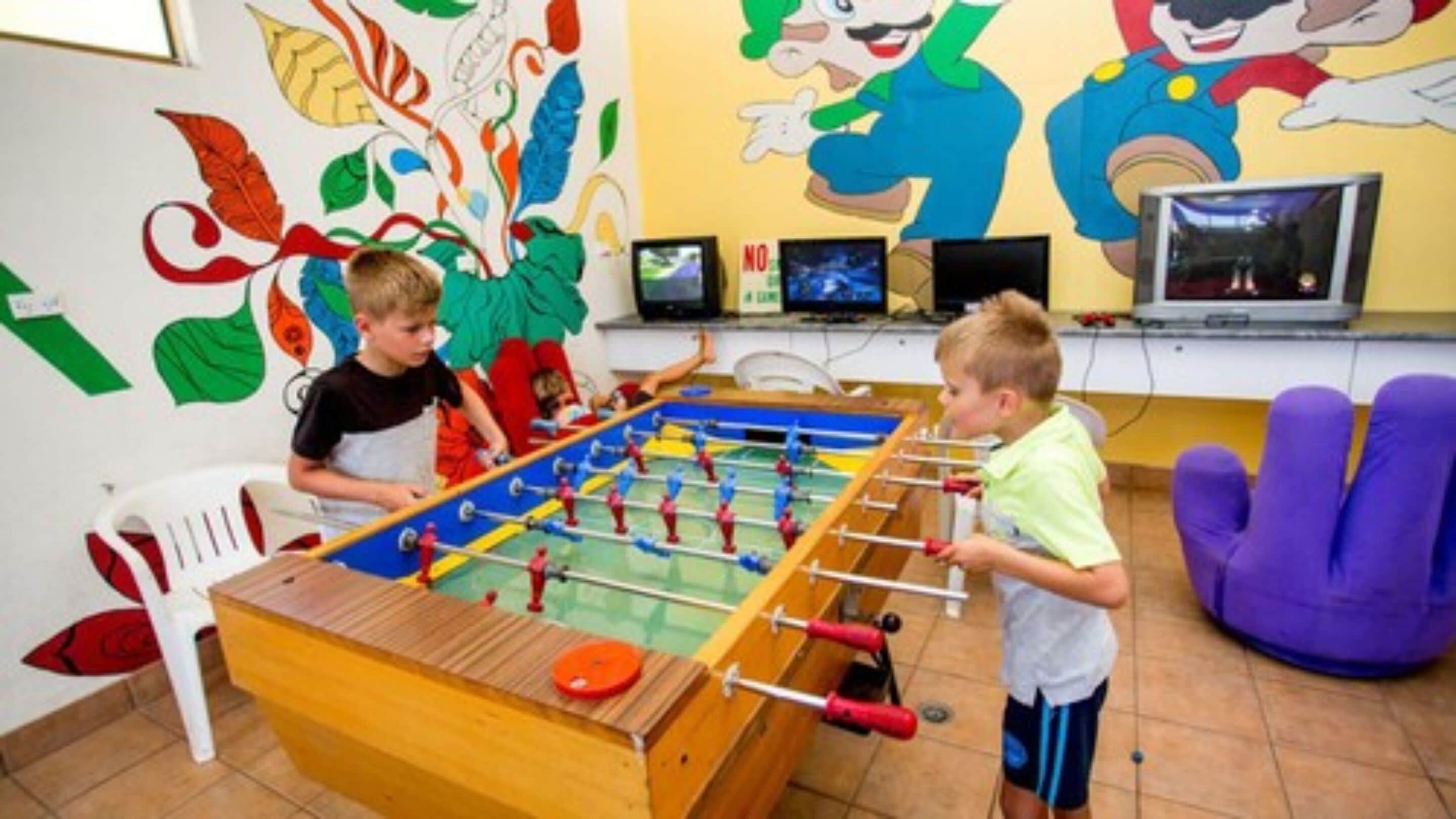 A room with a foosball table, a television, and colorful wall decorations.