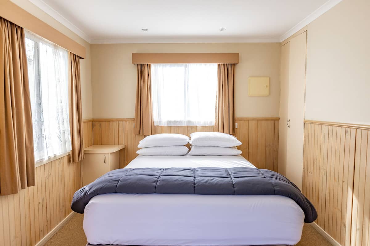 A bedroom with a bed, wooden walls, a window with curtains, and a bedside table.