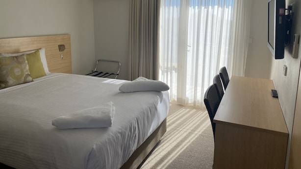 Une chambre d’hôtel avec un lit, un bureau, une chaise, une télévision et une fenêtre avec des rideaux.