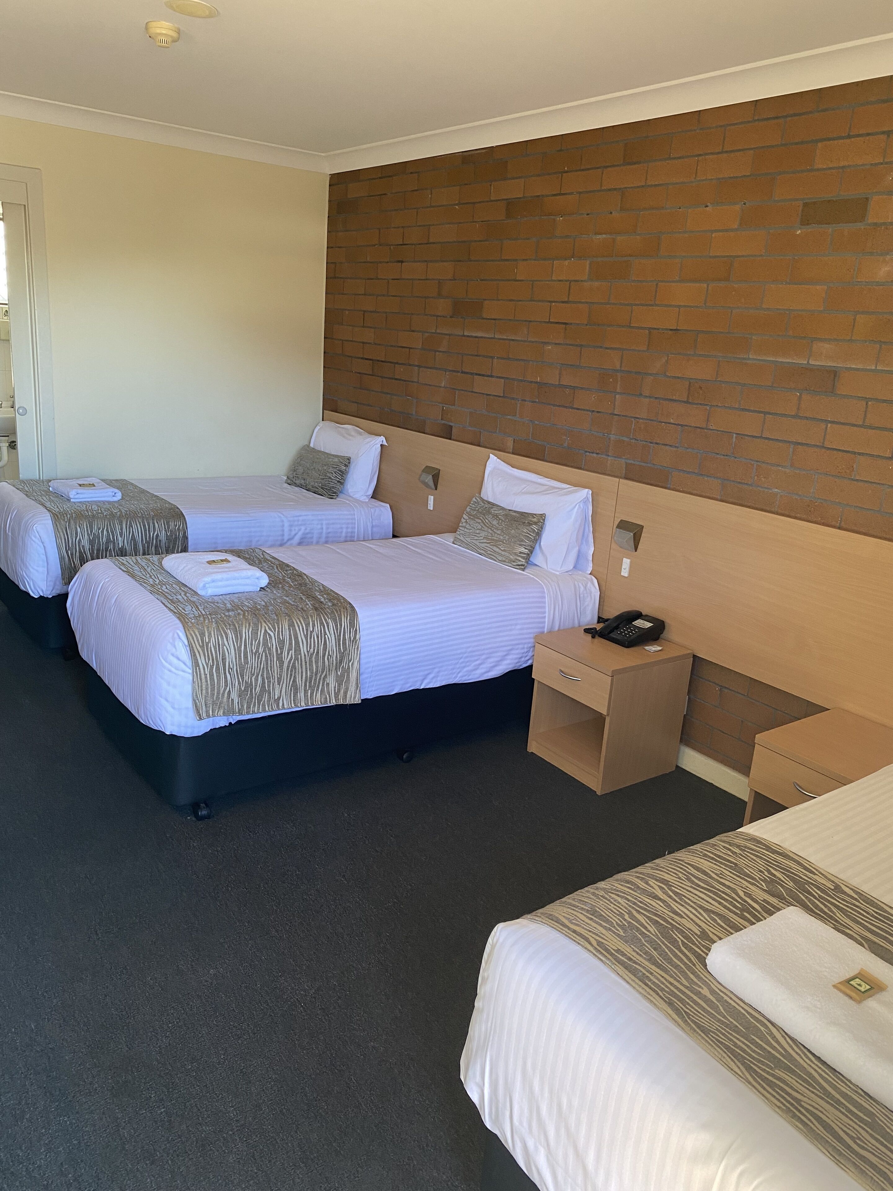 A hotel room with two beds, a wooden headboard, a bedside table with a phone, and a small desk.