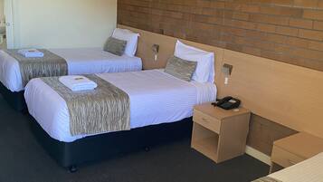 A hotel room with two beds, a wooden headboard, a bedside table with a phone, and a small desk.