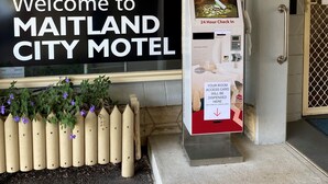 L’entrée du Maitland City Motel, avec un kiosque en libre-service et un panneau d’accueil.