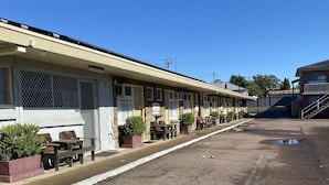 Une rangée de chambres de motel, chacune avec une entrée individuelle, des places assises à l’extérieur et un parking.