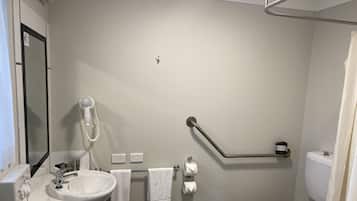 Un baño con lavamanos, espejo, toallero, inodoro y secamanos.