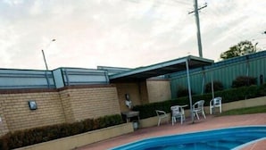 Une piscine à bord incurvé, entourée d’une terrasse carrelée et d’un espace salon couvert.