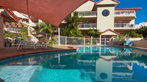A clear swimming pool with a tiled edge, surrounded by a white fence and palm trees.