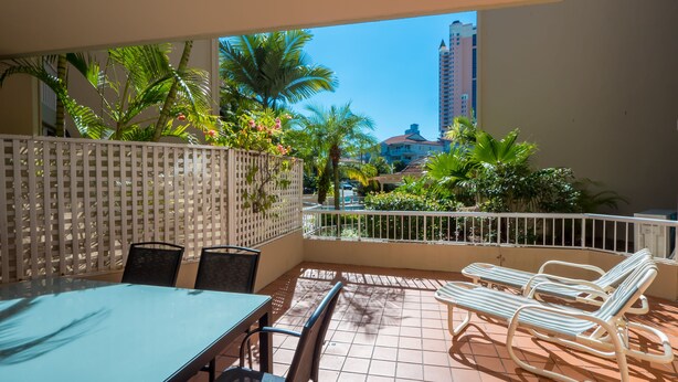 A balcony with a table and chairs, a white fence, and a view of palm trees and buildings.