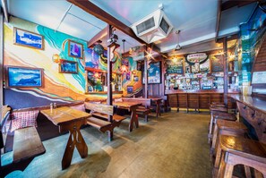 A bar with wooden benches and tables, colorful murals on the walls, and a variety of bottles and glasses on the shelves. - Airlie Court Units (Airlie Beach)