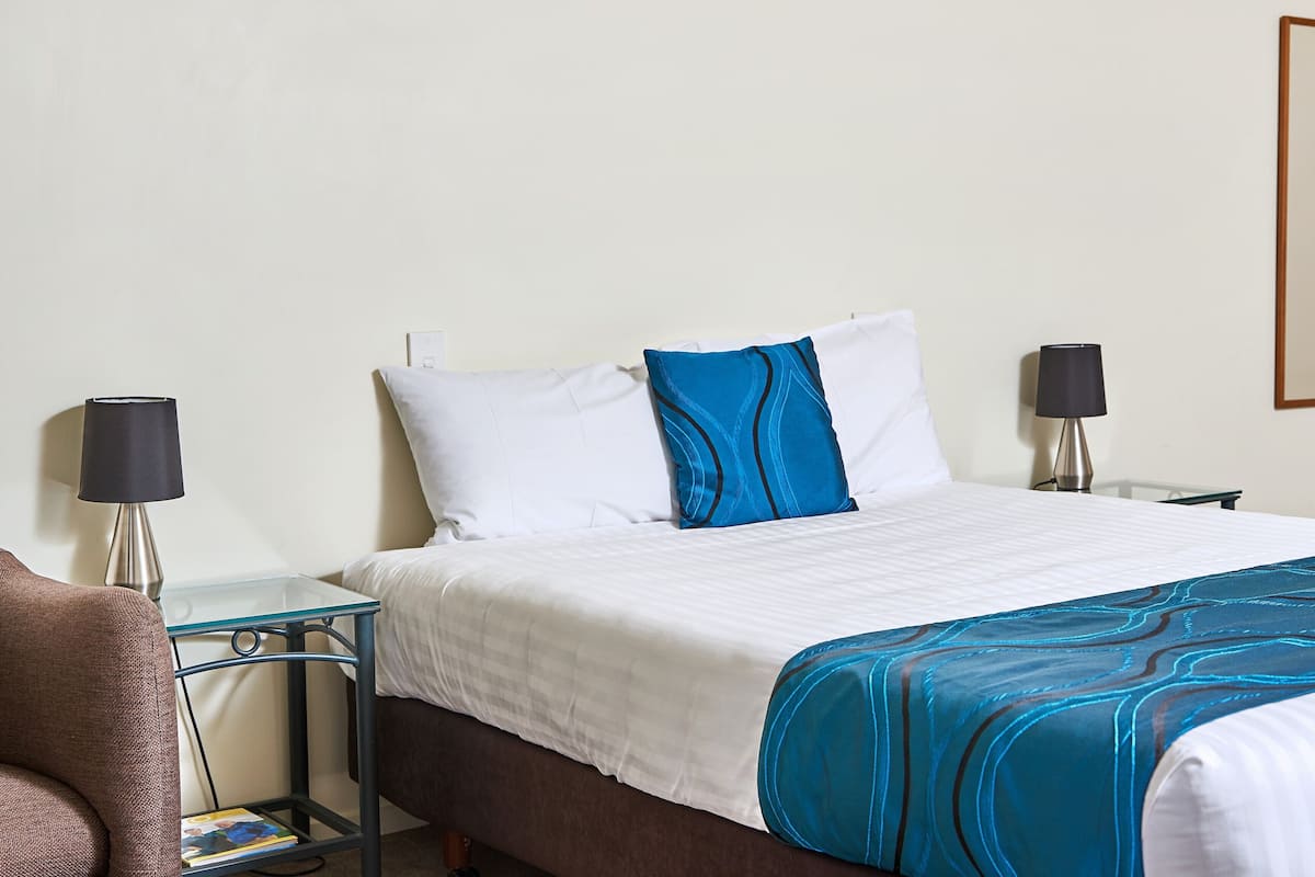 Una habitación de hotel con una cama, dos mesitas de noche, una lámpara en cada mesita y una silla.