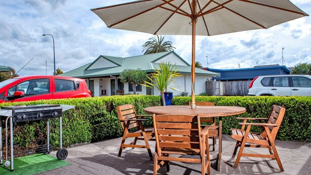 An outdoor seating area with a round wooden table and chairs, a large umbrella, and a barbecue grill.