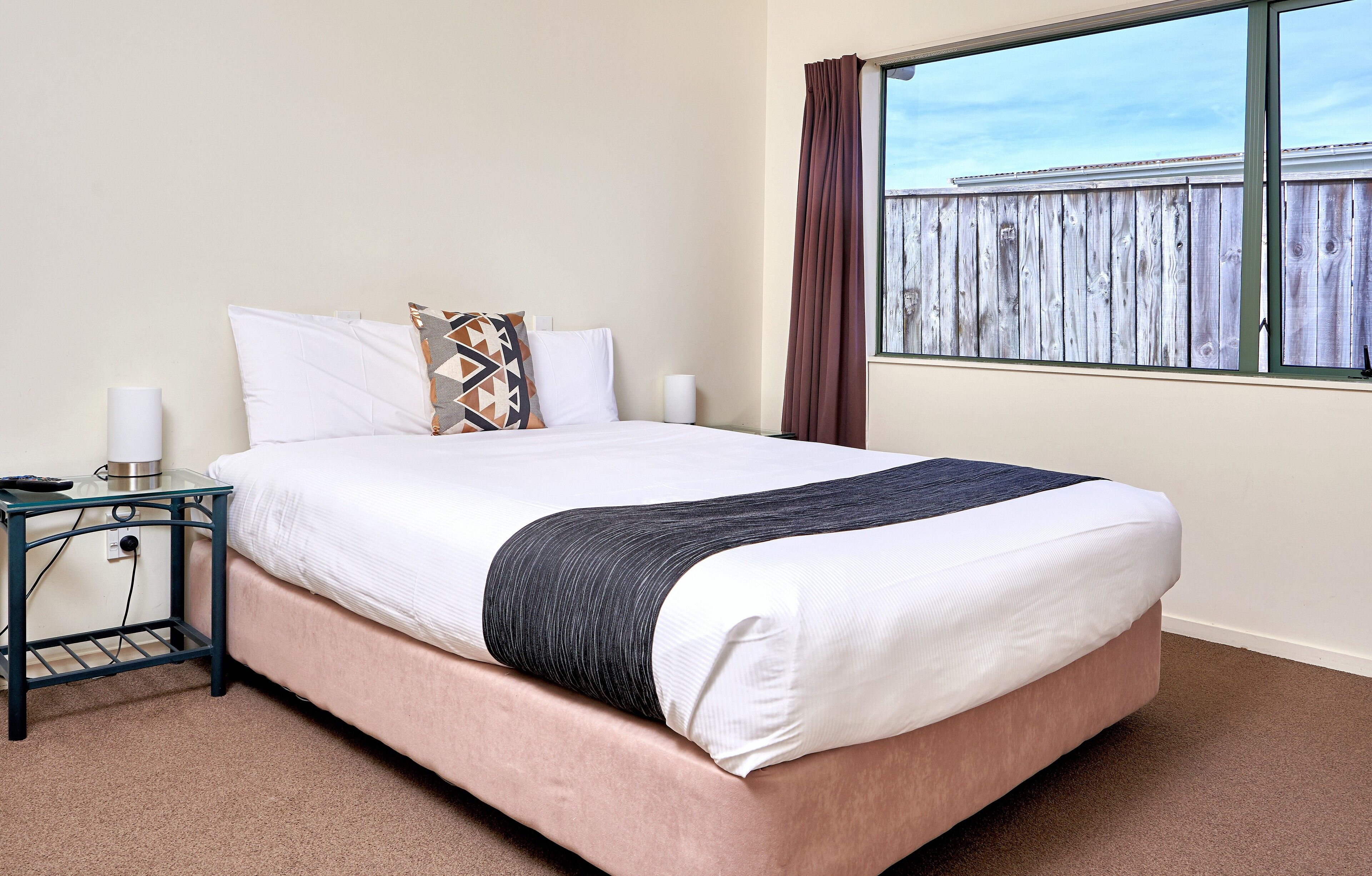 A neatly made bed with white and black bedding, a bedside table with a lamp, and a window with curtains.