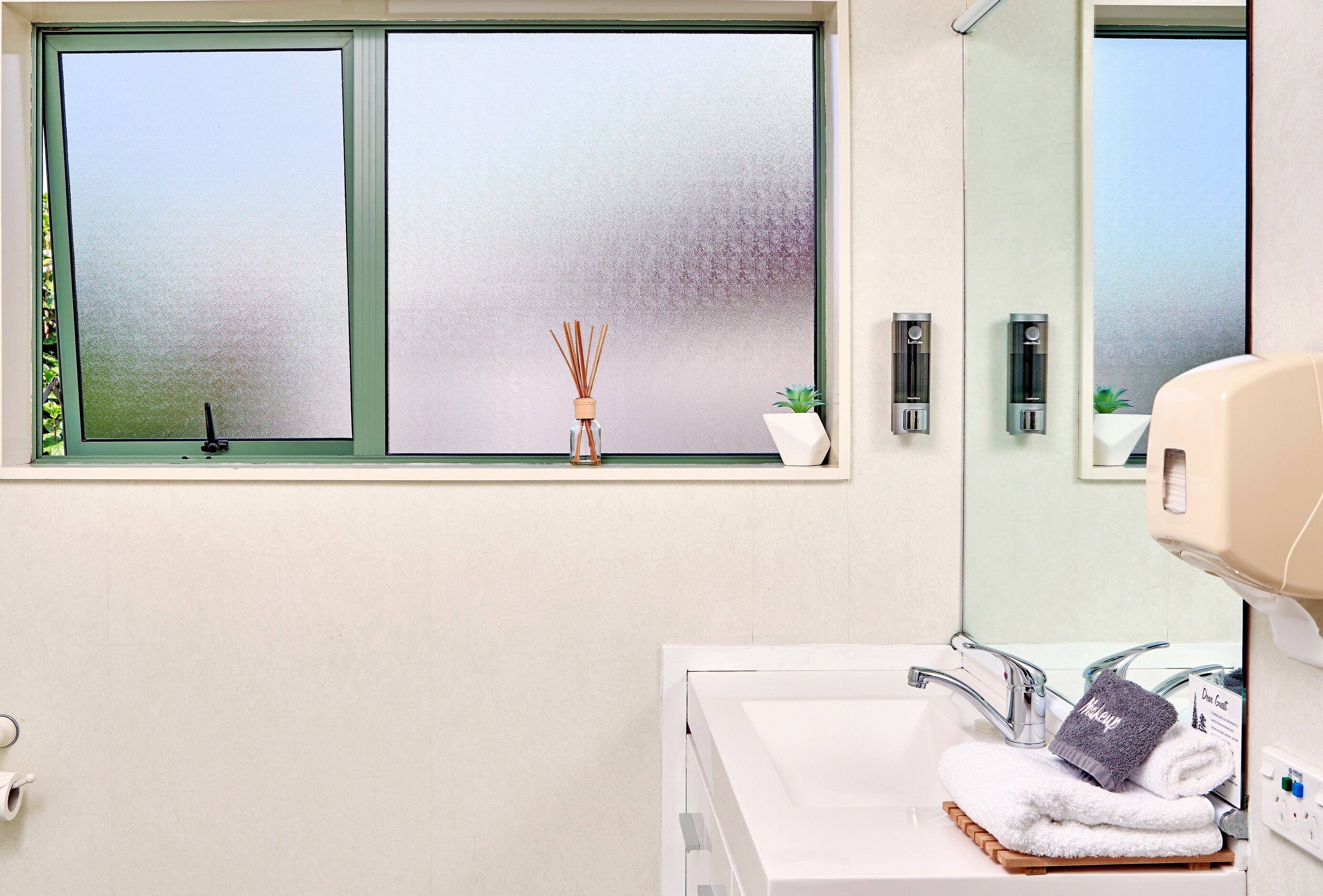 A bathroom with a window, a sink, a mirror, and a towel rack.