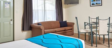 A hotel room with a bed, a sofa, a desk with a chair, a TV, and a window with curtains.