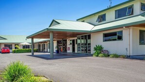 A two-story building with a covered entrance, a car parked in front, and a clear sky.
