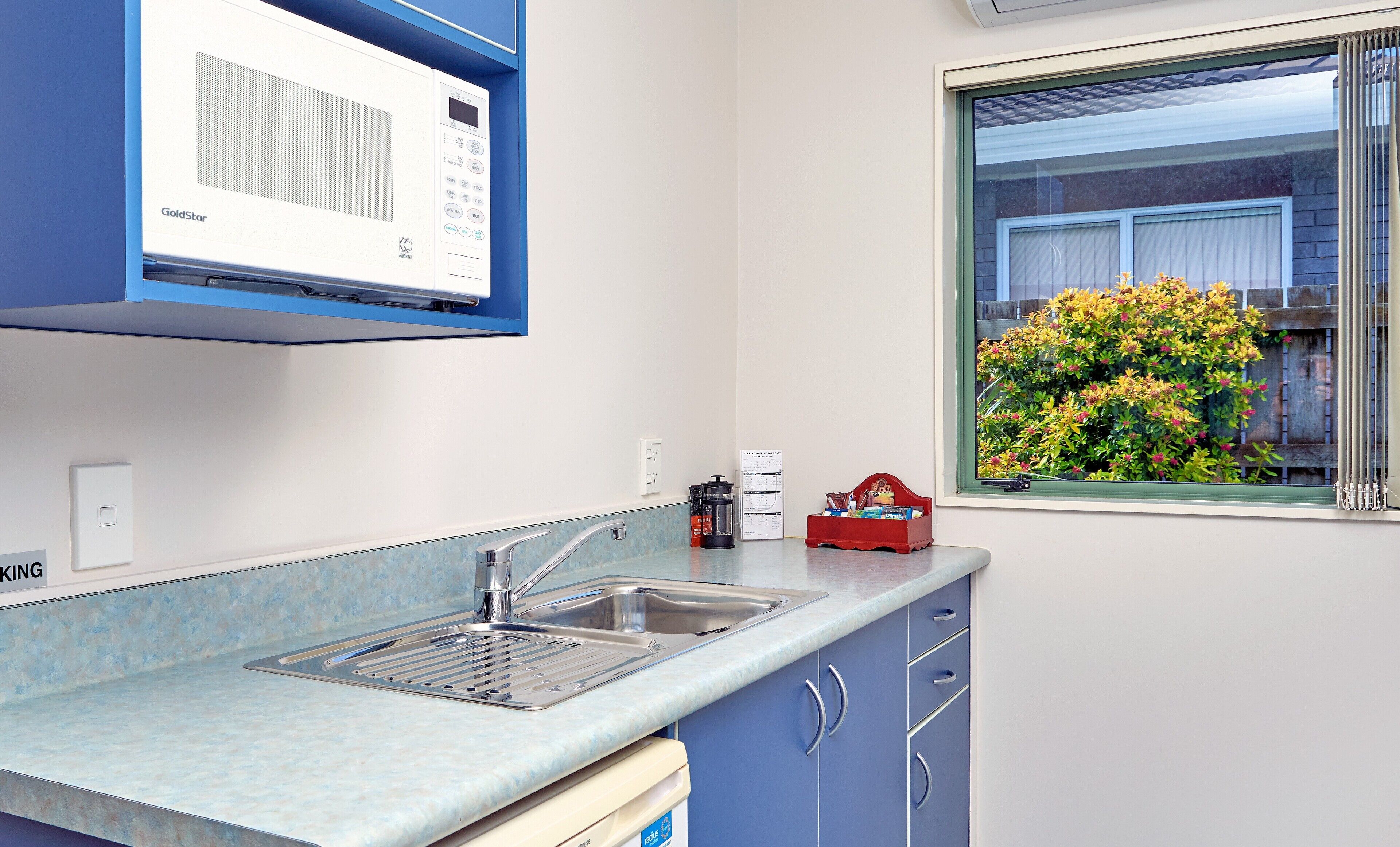 A modern kitchen with a built-in microwave, a stainless steel sink, and a window with a view of a garden.