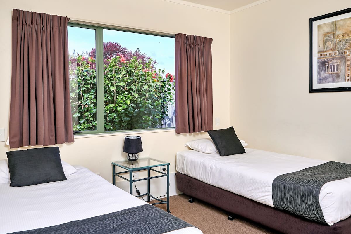 Habitación de hotel con dos camas, una mesita con lámpara, una ventana con cortinas y un cuadro en la pared.