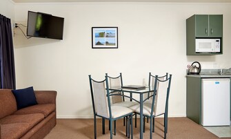 Un espacio habitable compacto con sofá, una mesa de comedor con sillas, televisor, un cuadro enmarcado, microondas y un refrigerador pequeño.