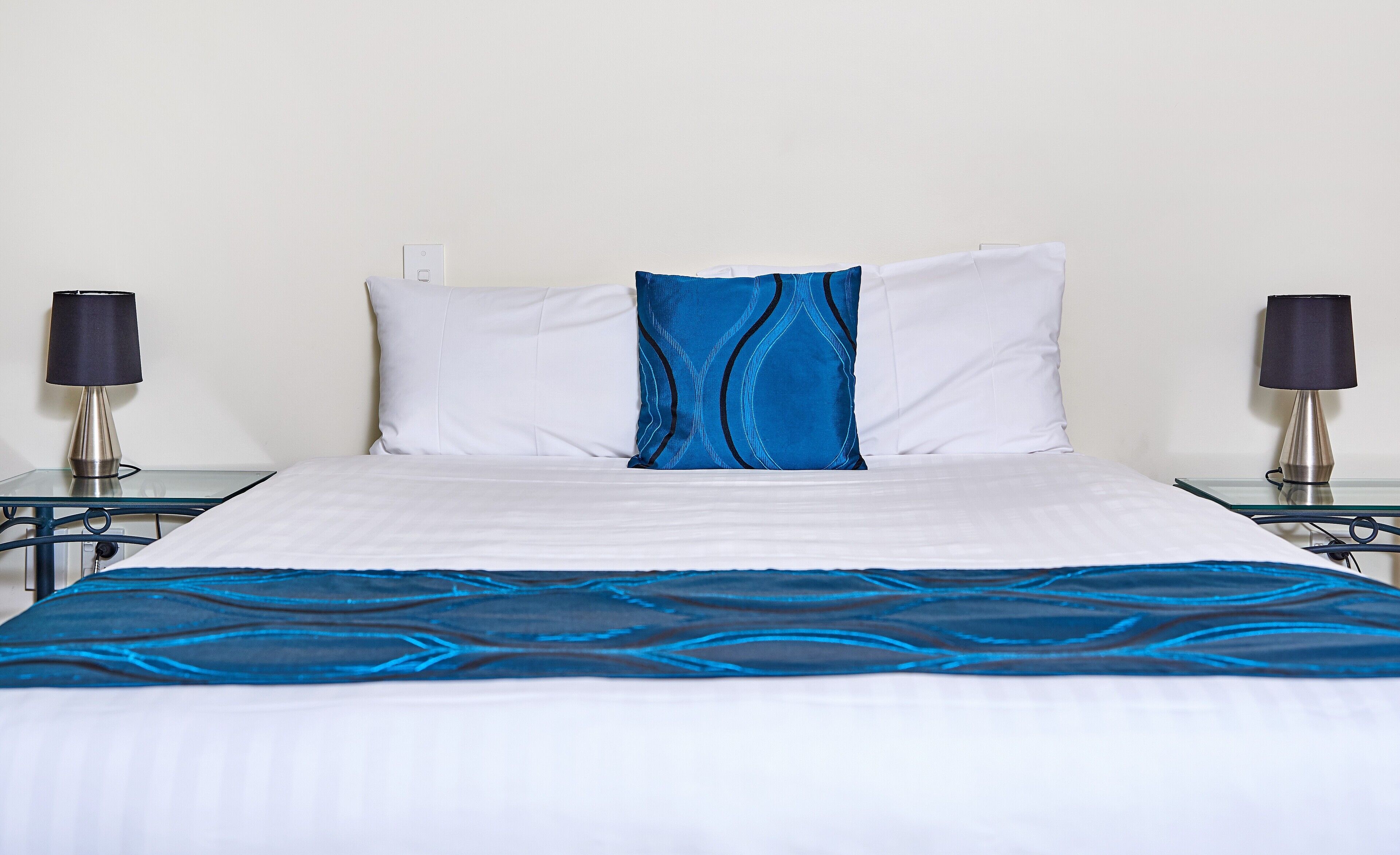 Una cama con una colcha blanca y azul, dos almohadas blancas y dos lámparas de noche.