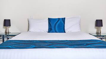 Una cama con una colcha blanca y azul, dos almohadas blancas y dos lámparas de noche.
