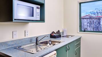 A compact kitchen with a built-in microwave, stainless steel sink, and a window with a view of a wooden fence.